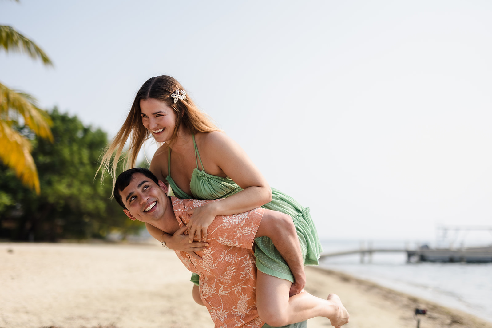 A couple piggybacks and laughs on Turtle Beach in Roatan on their couple's photoshoot by TKM Photography