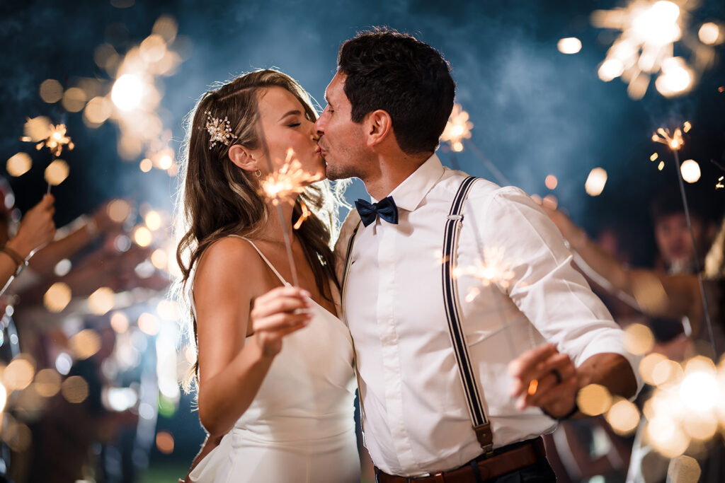 A couple kisses while surrounded by their friends and family holding sparklers in a sparkler tunnel at their Roatan wedding