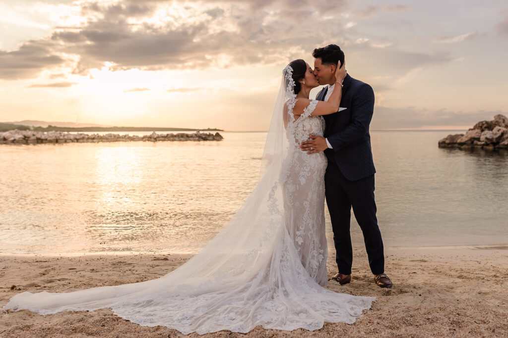 A bride and groom kiss on the beach at sunset on their wedding day by Roatan Wedding Photographers, TKM Photography