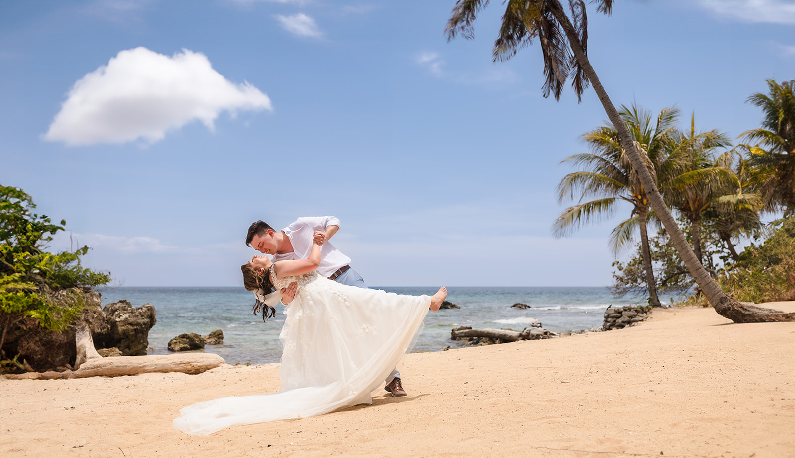 A bride and groom dip and kiss at their Roatan wedding on West Bay Beach