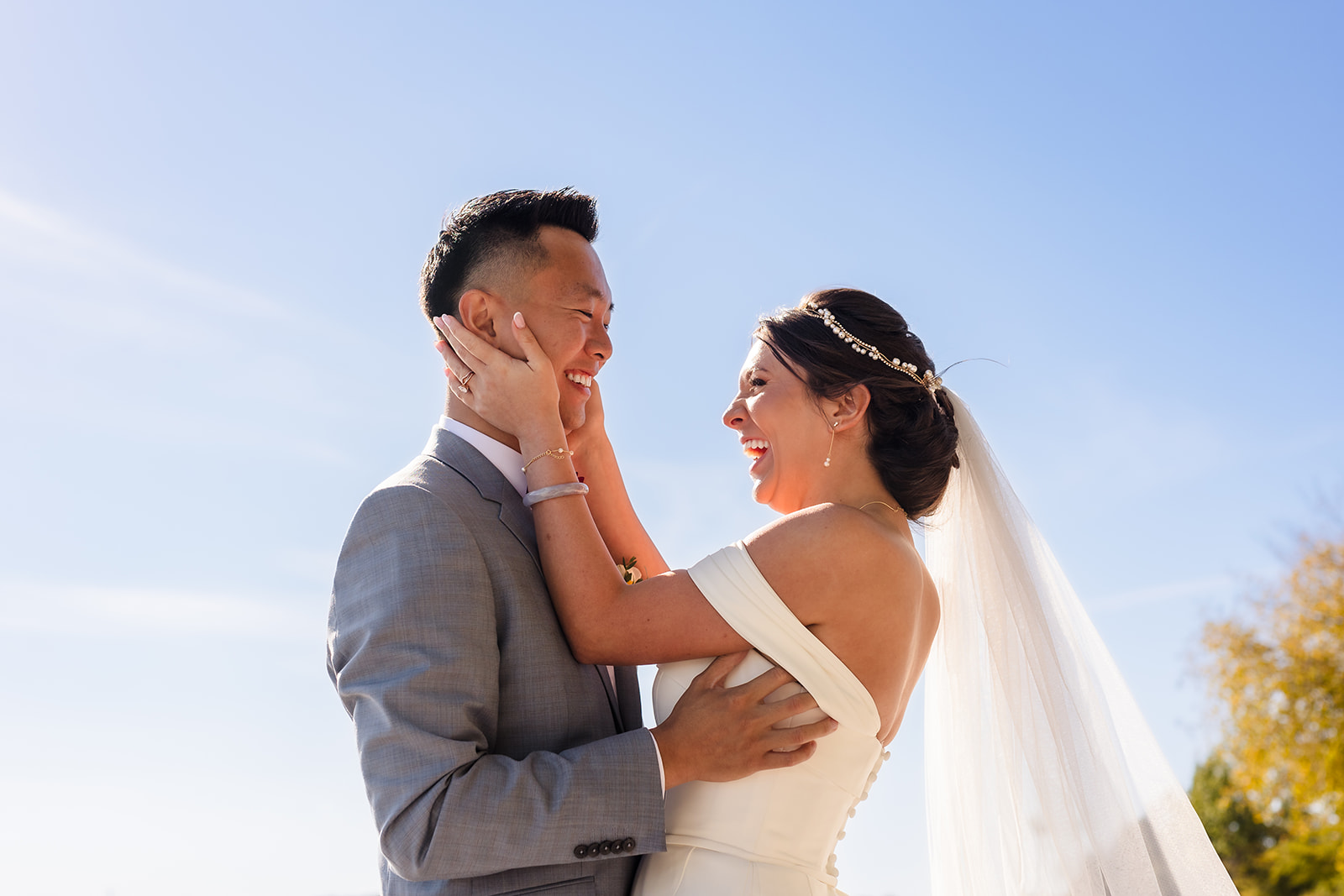 A bride holds her grooms face while they laugh together on a backdrop of a blue sky in Roatan