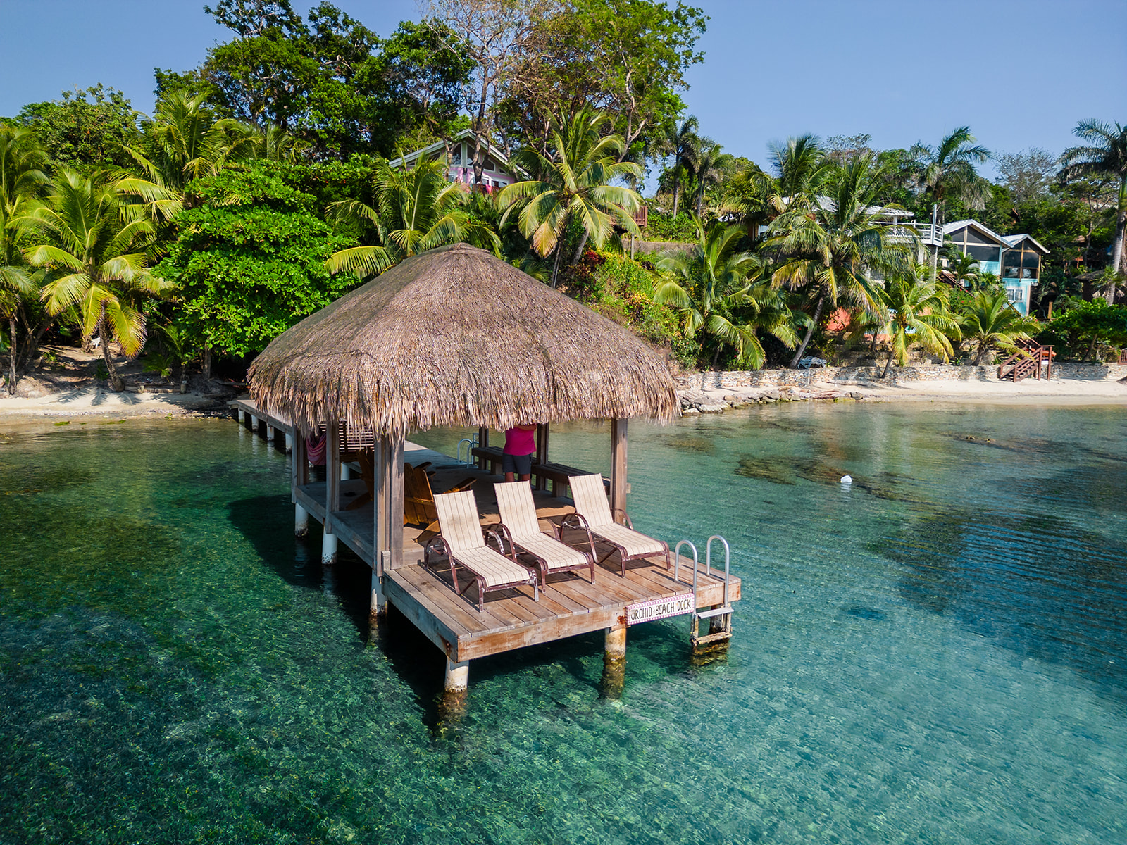 A cabana dock with three chairs is shown from a drone with Turtle Beach Roatan in the background