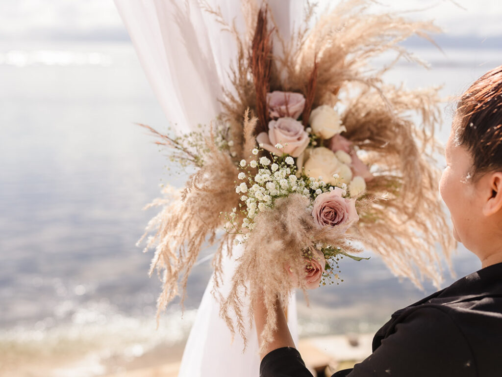 A florist, who is a Roatan wedding vendor, puts the finishing touches on a floral arch at a beach on Roatan