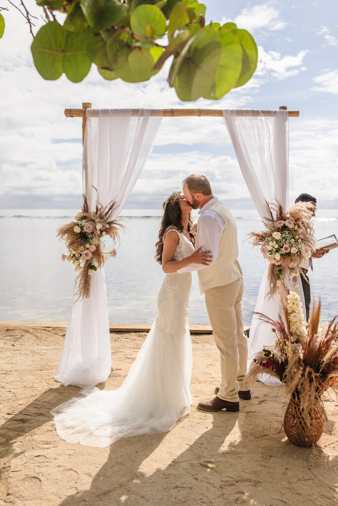 A bride and groom have their first kiss at their beachside wedding in Roatan under a boho floral arch.  