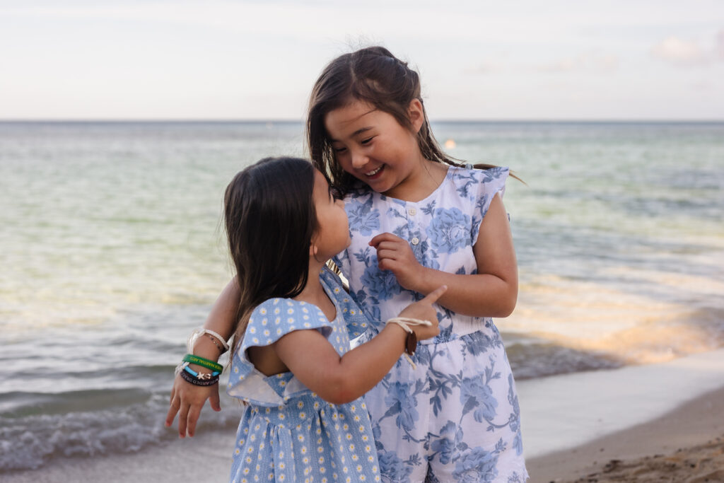 Young siblings (sisters) hugging on the beach.