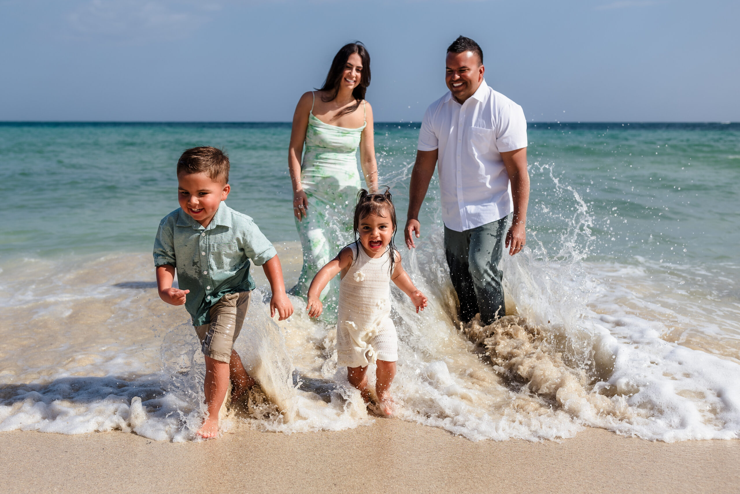 A couple chase their young children in the water on the beach.
