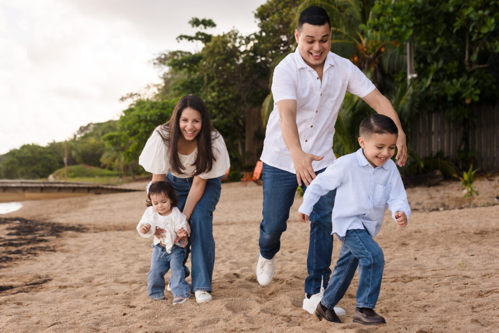 A couple chasing their young kids on the beach.