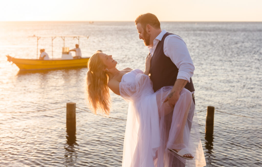 The groom dips his wife on the dock at sunset.