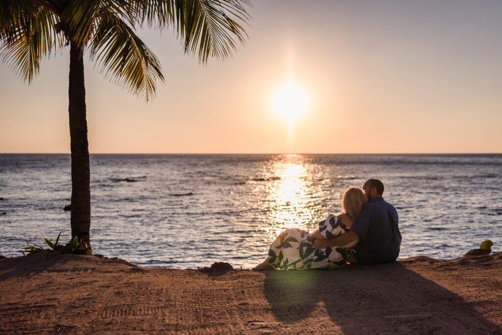 A couple sitting on the beach cuddling watching the sunset.