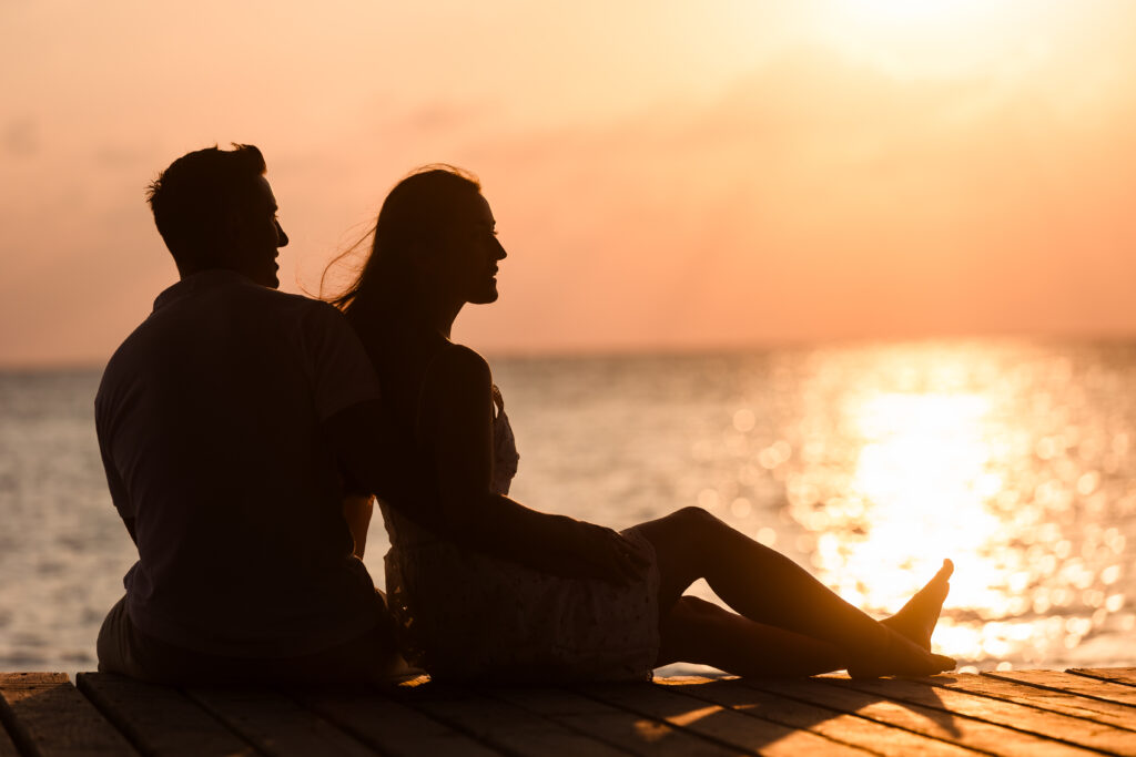 A couple sitting on the dock at sunset.