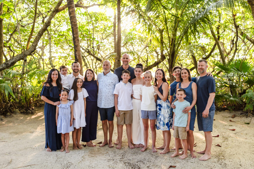 A large family smiling together on the beach.