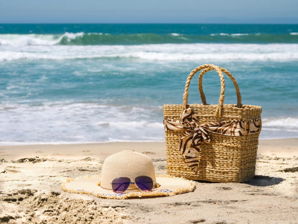 A beach tote and sun hat on the beach.