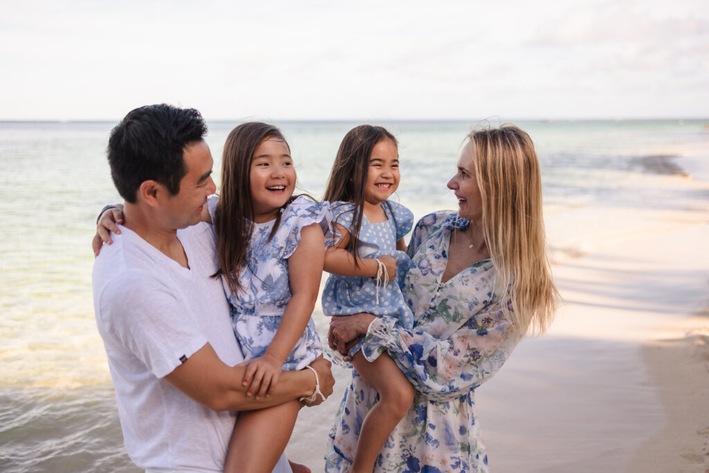 Parents holding their young daughters and smiling on the beach
