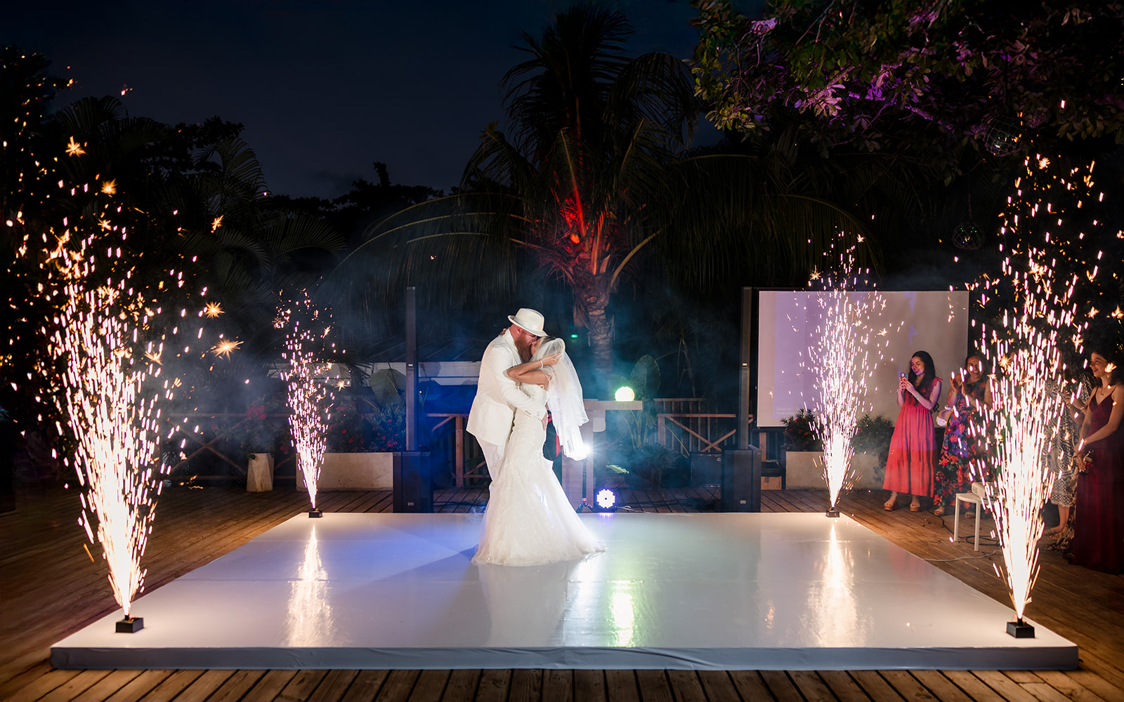A married couple embrace on the dance floor with sparklers going off around them.