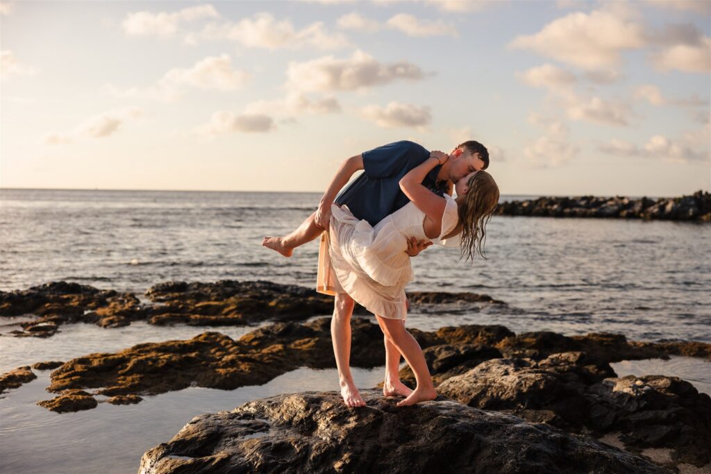 A man dips his fiance on a rock in the sea in Roatan after their Roatan proposal.
