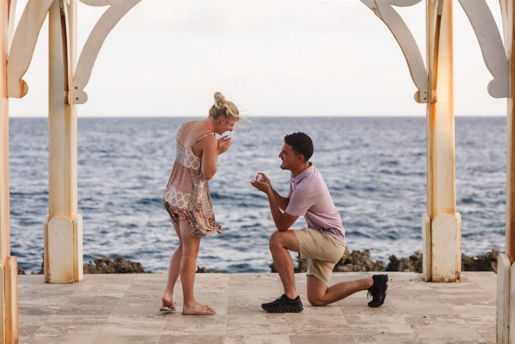 A woman laughs with joy while her boyfriend proposes to her on the iron shore in Roatan.