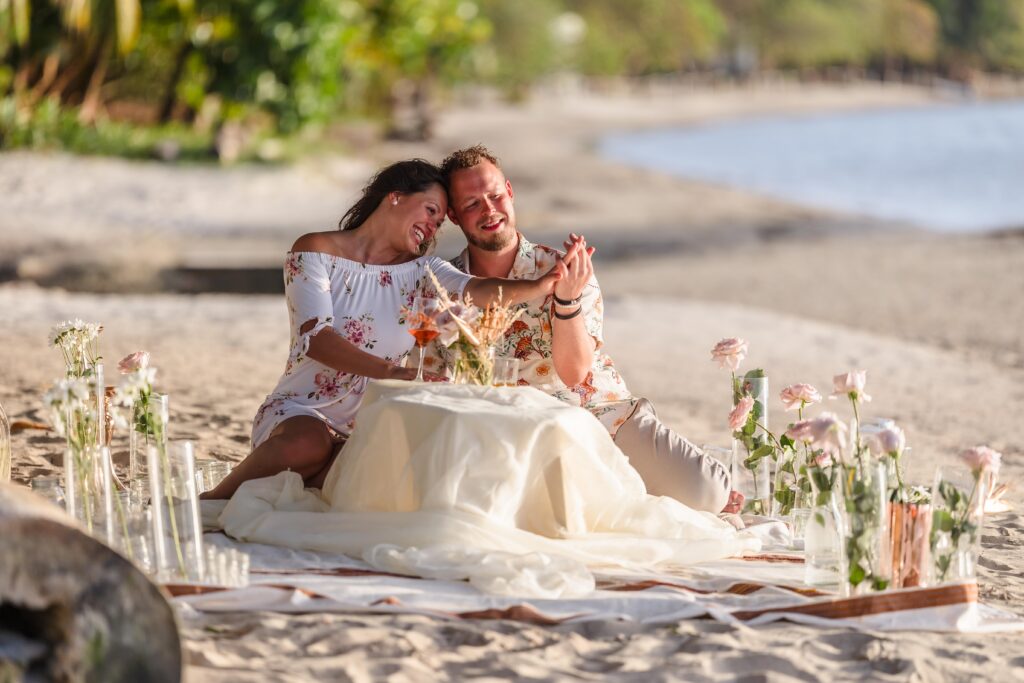 A just engaged couple admire her ring after their Roatan proposal sitting at a picnic setup.
