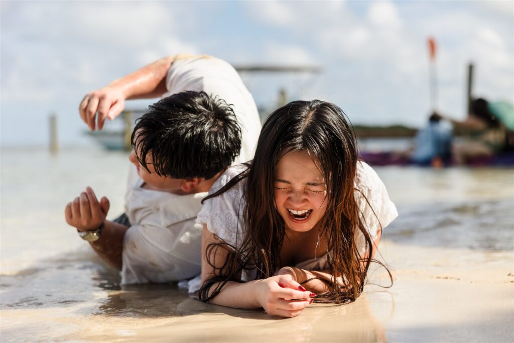 A couple laughs and plays on their stomachs in the ocean in Roatan after their Roatan proposal.
