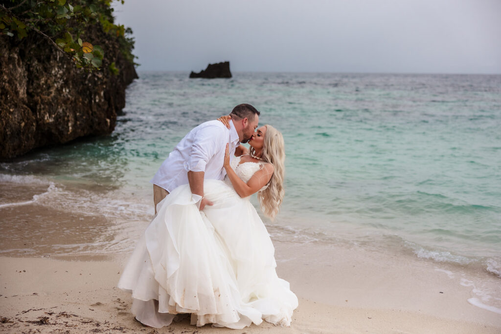 A couple kisses while she is being dipped on West Bay Beach at their Roatan trash the dress photo session. 