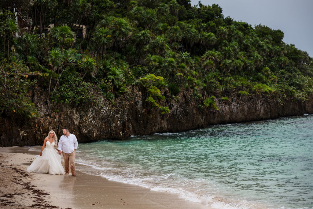 A couple walks on the beach during their Roatan trash the dress photo session