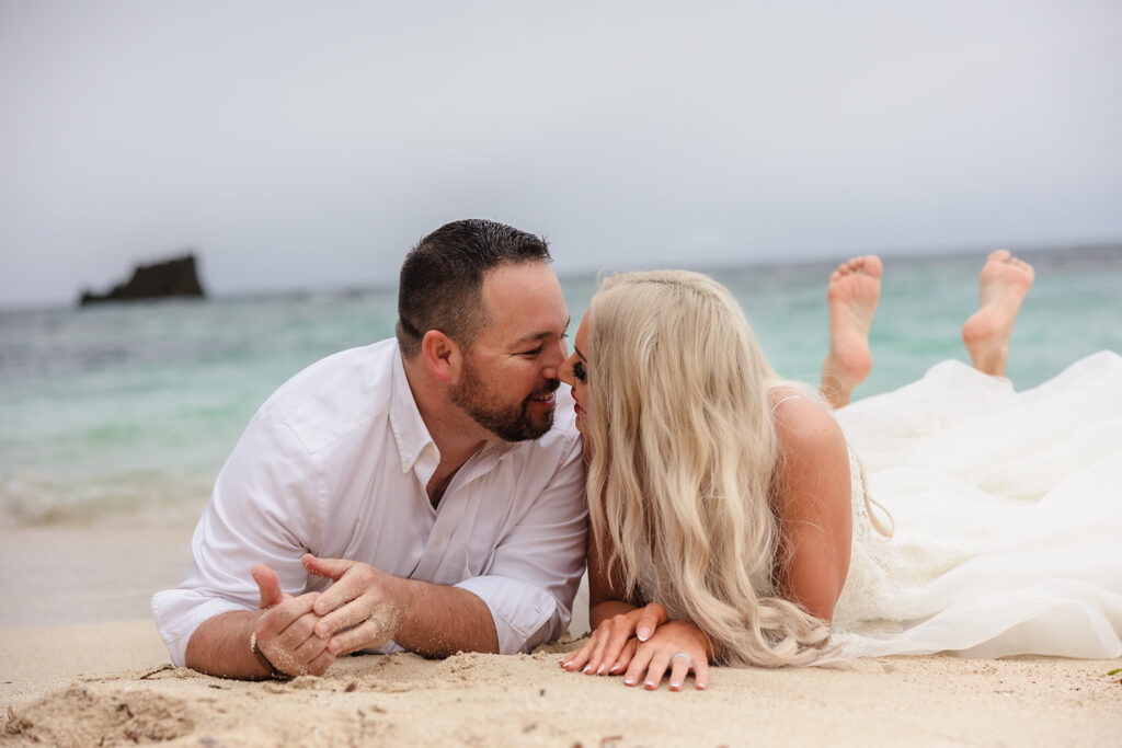 A couple lies in the sand on their stomachs at West Bay Beach during their Roatan trash the dress photo session.  