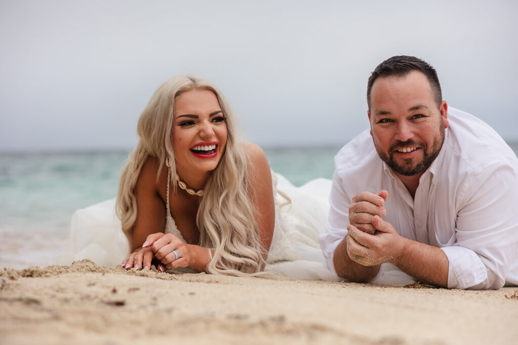 A couple lies in the sand on their stomachs at West Bay Beach during their Roatan trash the dress photo session.  