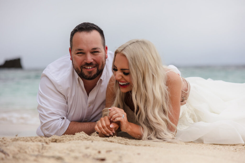 A couple lies in the sand on their stomachs at West Bay Beach during their Roatan trash the dress photo session.  