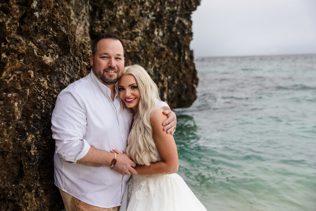 A couple hugs against the Iron Shore at West Bay Beach during their Roatan trash the dress photo session.  