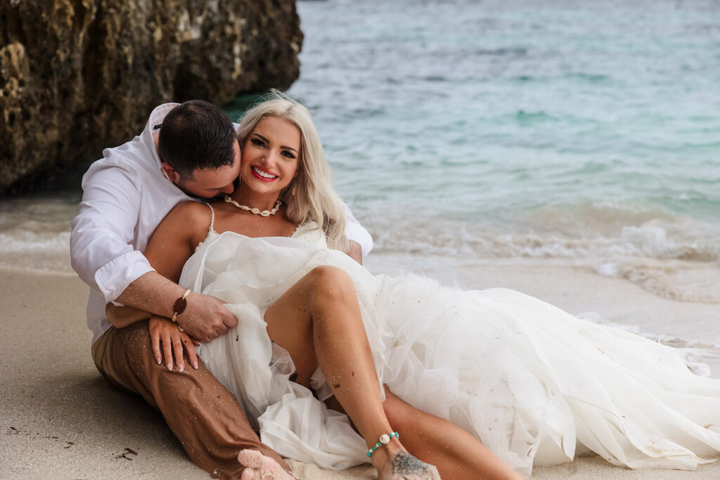 A couple lies in the sand at West Bay Beach during their Roatan trash the dress photo session.  