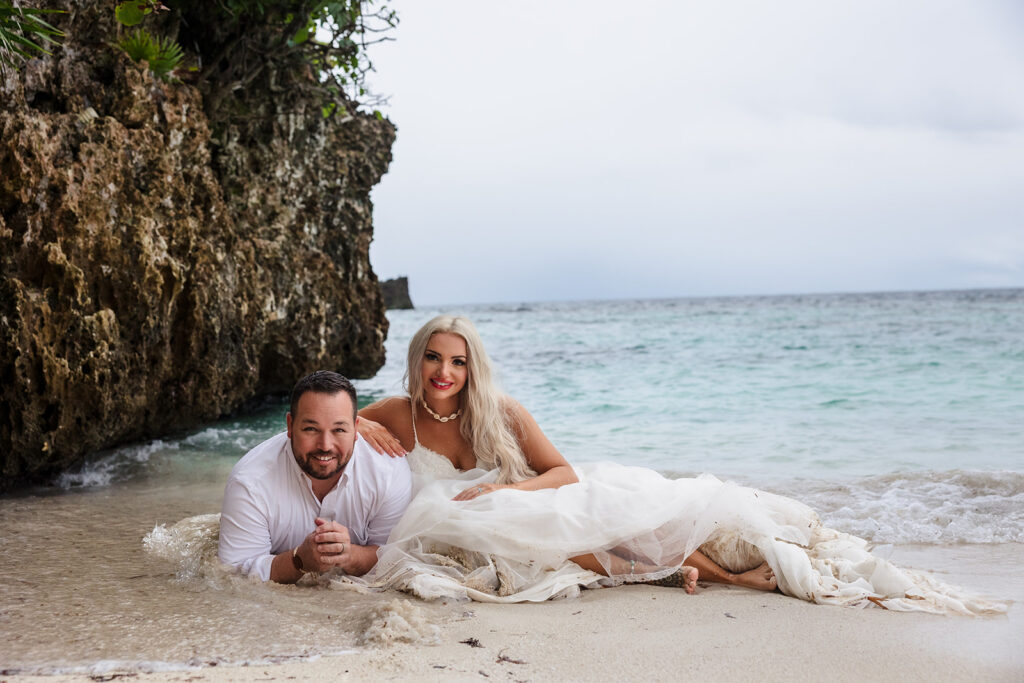 A couple lies in the sand at West Bay Beach during their Roatan trash the dress photo session.  